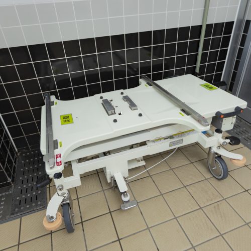 介護施設の機能訓練室に設置された医療用ベッド。白色のベッドフレームと黒白のタイル壁。